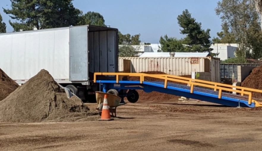 Work yard with a truck backed up to an portable heavy duty ramp.